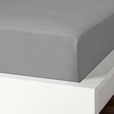 Una sábana bajera de algodón gris desplegada sobre una estructura de cama blanca, que muestra su textura suave y transpirable y su borde elástico.