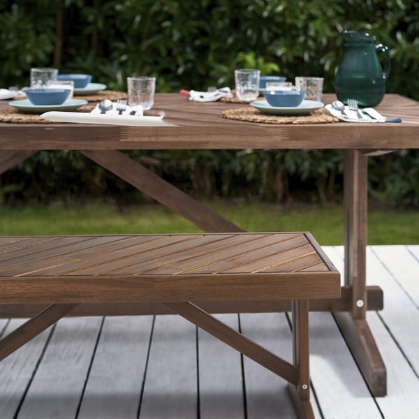 Mesa de comedor de exterior con estampado de espiga en acacia marrón. Se muestra con platos, tazones, vasos. Diseño rústico y robusto. Tamaño grande.