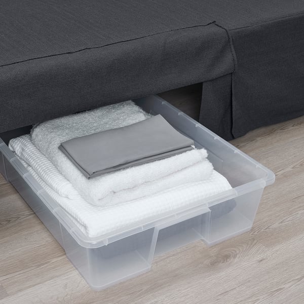 El contenedor transparente debajo del sofá almacena la ropa de cama doblada, maximizando el espacio.