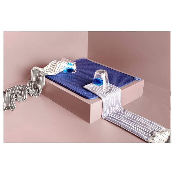 Alfombra de secado NYSKÖLJD en color azul, fabricada en poliéster reciclado, colocada sobre un bloque rosa con dos vasos de cristal.