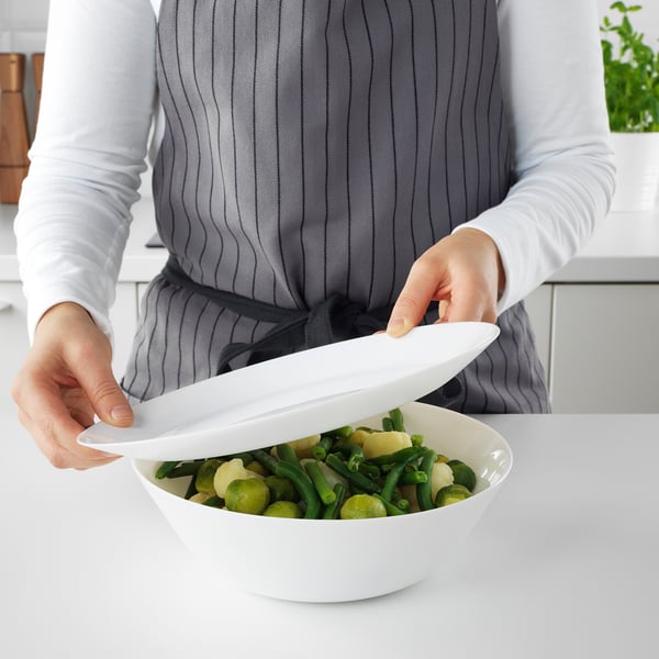 Persona colocando la tapa de un tazón de verduras mixtas sobre una encimera blanca.