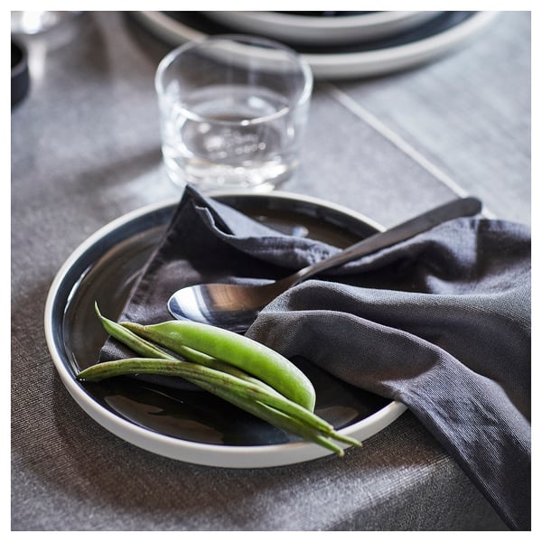 Plato oscuro con guisantes verdes y cuchara. Vaso y servilleta al lado. Diseño moderno y minimalista.