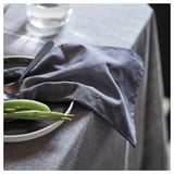 Servilleta oscura sobre mantel gris junto a verduras verdes sobre bol blanco.