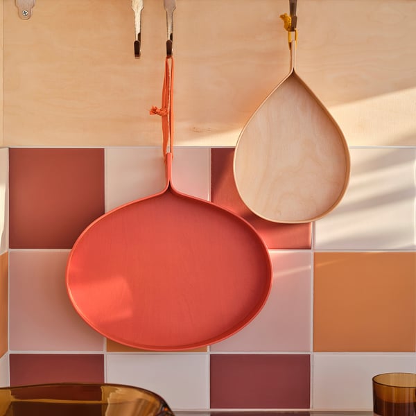 Dos bandejas de madera en forma de lágrima cuelgan contra una pared de azulejos de colores, perfectas para servir o exhibir.