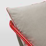 Un sillón moderno con cojines suaves, con una estructura de metal rojo brillante y cojines en tonos neutros con ribetes rojos, que ofrecen comodidad y estilo.