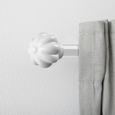 Remate de cortina de cerámica blanca que se asemeja a un capullo de flor, unido de forma segura a una cortina gris sobre una pared blanca.