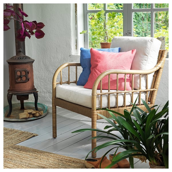 Acogedora sala de estar interior con silla de mimbre, almohadas de colores, plantas y un calentador de estufa sobre un piso de madera.