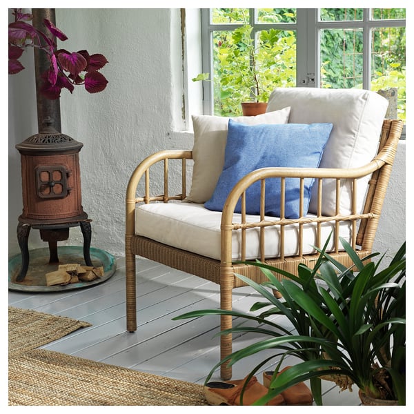 Acogedora silla de mimbre blanco con cojines azules y blancos, cerca de un calentador de ladrillo y rodeada de plantas.