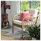 Acogedora sala de estar con silla de mimbre, cojines blancos y rosas, estufa de leña y plantas.