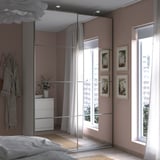 Dormitorio moderno con armario PAX con espejos, paredes rosas, muebles blancos, gran ventanal y cuadros florales.