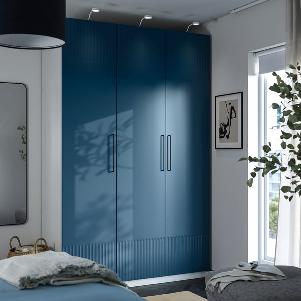 Dormitorio moderno con armario PAX azul, puertas reflectantes, cama y lámpara alta.