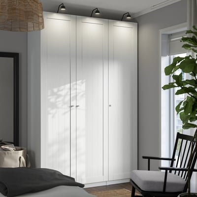 Dormitorio minimalista con gran armario PAX, paredes gris oscuro, lámpara colgante, mecedora y planta.