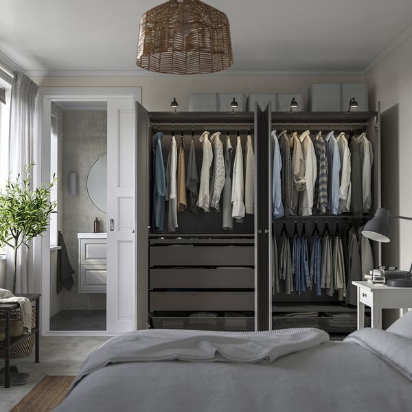 Dormitorio moderno con armario abierto con camisas y cajones; ropa de cama gris, lámpara de mimbre, planta.