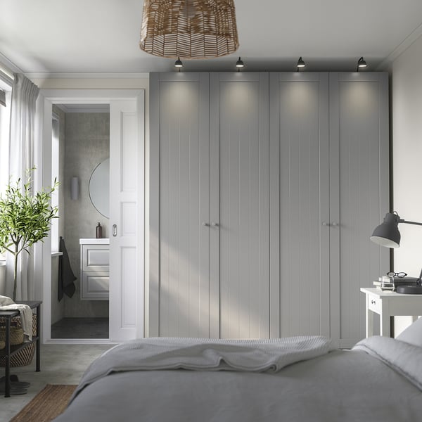 Dormitorio moderno con gran armario PAX gris, cama, planta. El armario tiene puertas iluminadas, paredes de color gris claro, decoración minimalista.