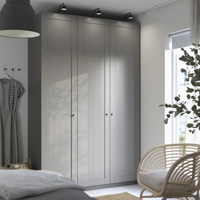 Dormitorio moderno con gran armario PAX en color gris, tres puertas, iluminación integrada, unidad oscura, cama grande, silla y planta.