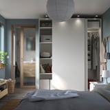 Un dormitorio moderno y minimalista con armarios blancos PAX con puertas correderas, una lámpara colgante y una cama bien hecha.