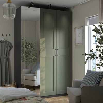 Dormitorio moderno, un gran armario verde PAX con puertas con espejos, erguido junto a un acogedor sofá y junto a una ventana, con sutiles paredes de color verde grisáceo.