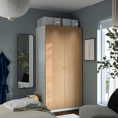 Dormitorio moderno con armario PAX, pared azul y planta junto a la ventana.