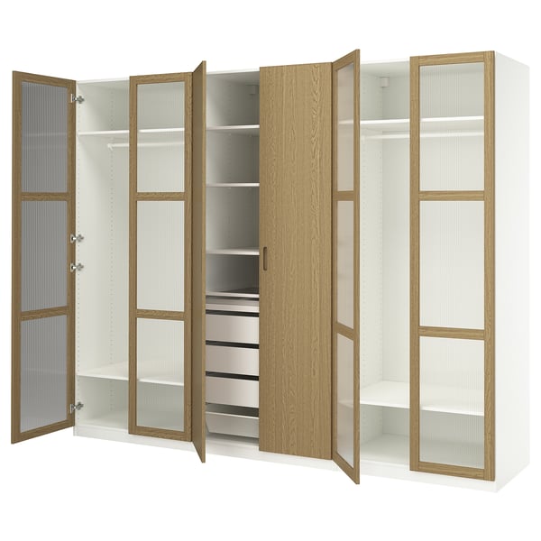 Esta imagen muestra un armario PAX blanco con puertas de chapa de roble, estantes de vidrio y cajones de metal. Cuenta con barras de ropa y compartimentos ajustables.
