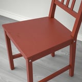 Silla de madera roja con listones verticales sobre suelo claro.