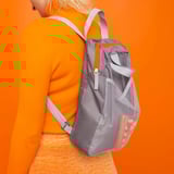 Persona vestida de punto naranja, que lleva una mochila PIVRING gris con bolsillo de malla sobre fondo naranja brillante.