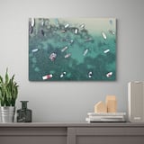 Un lienzo montado en la pared representa barcos aéreos en aguas oceánicas poco profundas, flanqueados por una planta, un jarrón decorativo, libros y un altavoz en un estante debajo.