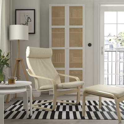 Salón moderno con silla POÄNG blanca, alfombra a rayas, lámpara y planta.