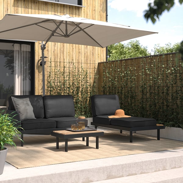 Conjunto de patio: sofá negro, mesa de centro y tumbona; casa de madera, vegetación; Gran paraguas beige.