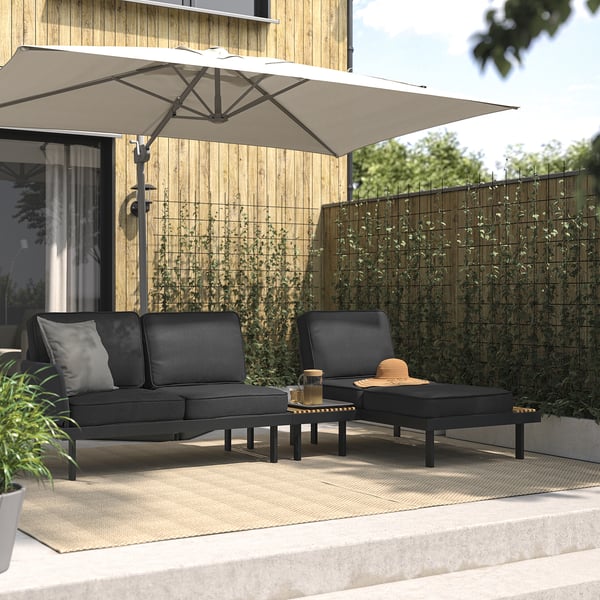 Moderno conjunto de salón al aire libre: sofá negro, mesa de centro y chaise con mesa auxiliar integrada bajo una gran sombrilla beige sobre una cubierta de madera.