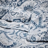 Ropa de cama plegada con estampado de cachemira azul y blanco con botones forrados en tela, que luce su diseño decorativo y funcional.