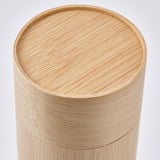 Recipiente cilíndrico de bambú con acabado liso y envejecido. La tapa se ajusta perfectamente, evocando el almacenamiento tradicional de té. El recubrimiento de laca transparente realza el grano natural.