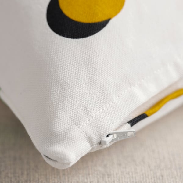 Primer plano de una funda de cojín blanca con un gran círculo amarillo y negro, detalle de cremallera visible.