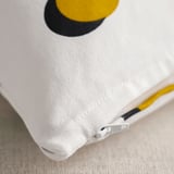 Primer plano de una funda de cojín blanca con un gran círculo amarillo y negro, detalle de cremallera visible.