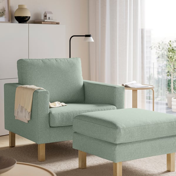 Sillón verde y otomán en el salón moderno. Mesita auxiliar y estantería con decoración.
