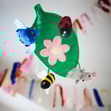 Móvil colorido con búho, mariquita, abeja y ratón que cuelga de una hoja verde con flor, estimulando la visión y la curiosidad del bebé.