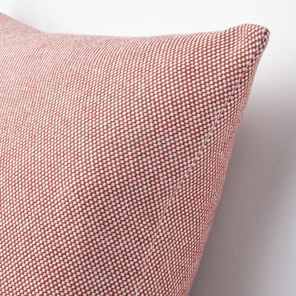 Cojín rojo y blanco con textura tejida, colocado sobre una superficie blanca. La cubierta tiene un patrón táctil detallado.