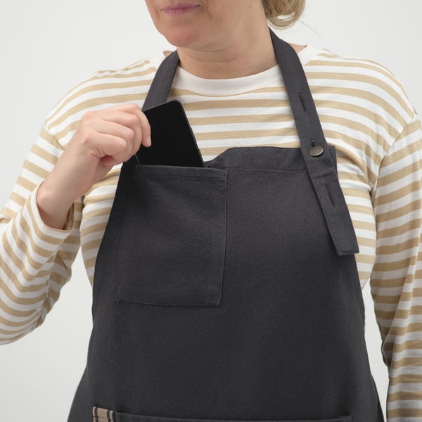 Persona que viste una camisa a rayas y un delantal negro. El delantal tiene cuello ajustable, prácticos bolsillos y lazo para colgar herramientas.