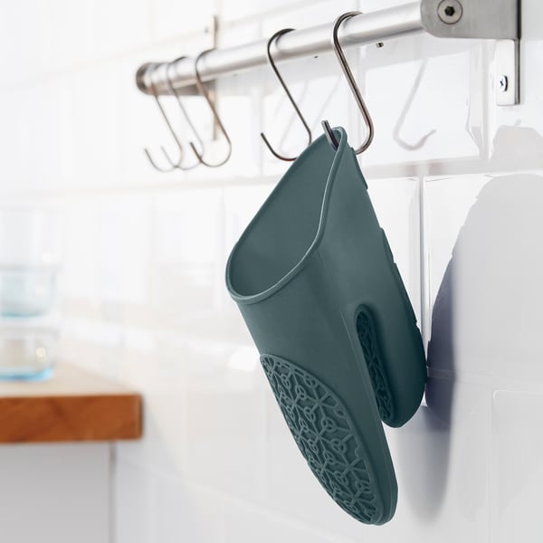 El guante de cocina verde azulado cuelga del gancho de la cocina, diseñado para proteger contra el calor y facilitar el almacenamiento.