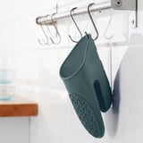 El guante de cocina verde azulado cuelga del gancho de la cocina, diseñado para proteger contra el calor y facilitar el almacenamiento.