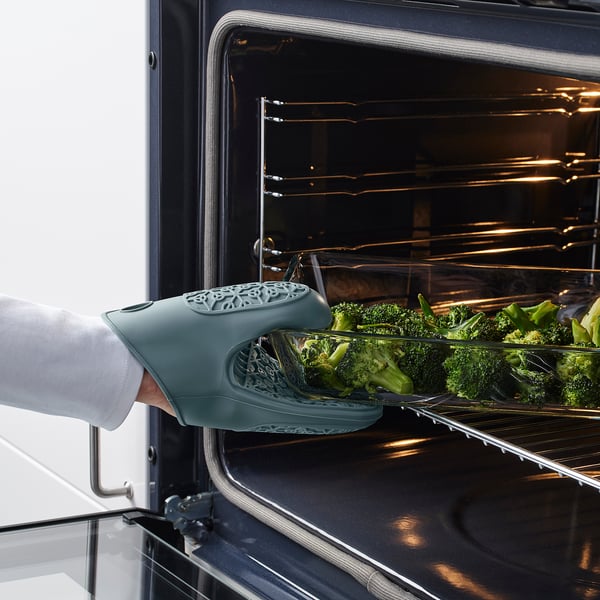Persona colocando una bandeja de brócoli en el horno con un guante de silicona verde para horno.