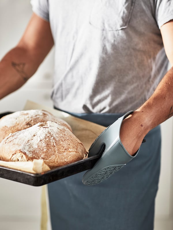Una persona usa un guante de horno gris de silicona para manejar una bandeja para hornear con pan artesanal.