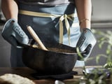 Una persona con delantal y guantes de cocina sostiene la sartén con la comida, cocinando.