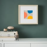 Arte abstracto en pared verde con formas azules, naranjas, amarillas. Abajo, estantería blanca con figuras y libros de madera.