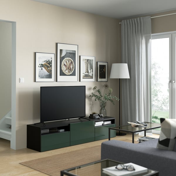 Sala de estar moderna con mueble de TV verde oscuro, cajones, mesa de centro de vidrio, cortinas grises y decoración.
