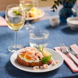 Plato con aperitivo de camarones, copa de vino, utensilios, mantel azul.