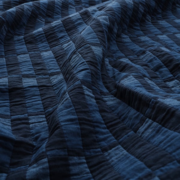 Edredón azul oscuro con costuras visibles, cuidadosamente doblado, que muestra tela de calidad y artesanía.