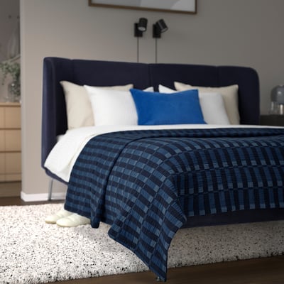 Ropa de cama y fundas de almohada a cuadros azul marino Skogsskovall en cama king con cabecero azul oscuro y alfombra blanca