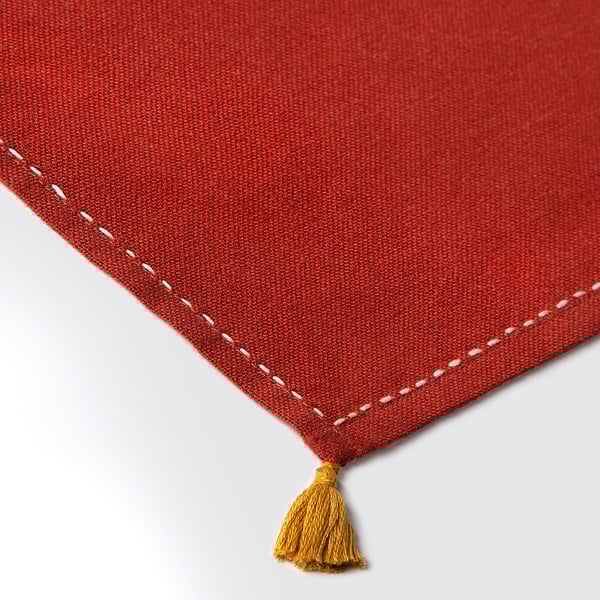 Servilleta tejida roja con bordes cosidos a mano y borlas amarillas, que muestra artesanía de alta calidad.