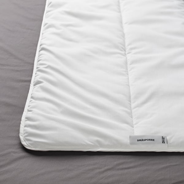 Un primer plano de un edredón blanco sobre una cama, que muestra su textura suave y afelpada y la etiqueta de la esquina que muestra SMÅSPORRE.