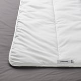 Un primer plano de un edredón blanco sobre una cama, que muestra su textura suave y afelpada y la etiqueta de la esquina que muestra SMÅSPORRE.